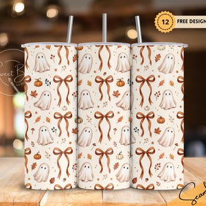 May include: A cylindrical tumbler with a straw featuring a repeating pattern of white ghosts, orange pumpkins, brown bows, and autumn leaves on a cream background. The design includes small berries and acorns scattered across the surface.