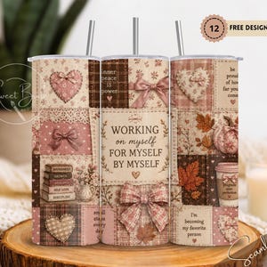 May include: A cylindrical tumbler with a straw featuring a patchwork design in shades of brown, pink, and cream. The pattern includes hearts, bows, autumn leaves, a pumpkin, a coffee cup, and text reading "WORKING on myself FOR MYSELF BY MYSELF."