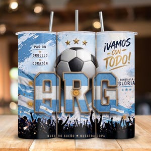 May include: A cylindrical tumbler with a straw featuring a soccer theme, the letters ARG in blue and white, a soccer ball, three gold stars, and the text PASI&Oacute;N, ORGULLO, CORAZ&Oacute;N, &iexcl;VAMOS CON TODO!, and RUMBO A LA GLORIA, with a crowd silhouette at the base.