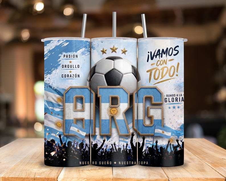 May include: A cylindrical tumbler with a straw featuring a soccer theme, the letters ARG in blue and white, a soccer ball, three gold stars, and the text PASI&Oacute;N, ORGULLO, CORAZ&Oacute;N, &iexcl;VAMOS CON TODO!, and RUMBO A LA GLORIA, with a crowd silhouette at the base.