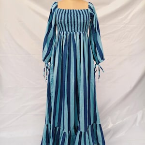 Könnte beinhalten: Ein langes, blau-türkis gestreiftes Kleid mit quadratischem Ausschnitt und langen Ärmeln. Das Oberteil ist gerüscht und die Ärmel haben Bindebänder an den Handgelenken. Das Kleid hat einen Rüschensaum und wird auf einer Schaufensterpuppe präsentiert.