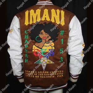 Op de afbeelding: Bruin en witte varsity jas met geborduurde details. De achterkant heeft het woord "IMANI" in geel, een afbeelding van een vrouw en de tekst "CHAPTER OES". Extra tekst omvat "#153" en "EURKA GRAND CHAPTER ORDER OF THE EASTERN STAR STATE OF ILLINOIS, PHA".