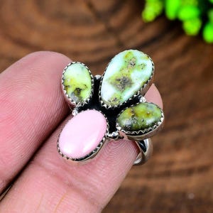 Peut inclure: Une bague en argent ornée d'un groupe de pierres précieuses. La bague présente quatre pierres ovales de nuances vertes et une pierre ovale rose. Les pierres sont serties dans un sertissage en métal argenté.