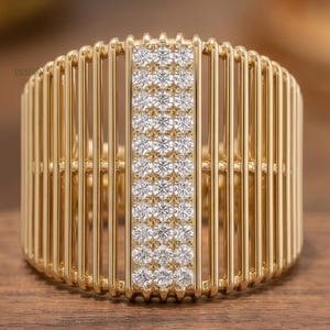 Könnte beinhalten: Ein goldfarbener Ring mit vertikalen Stäben und einer zentralen Reihe kleiner, funkelnder Steine. Der Ring ist auf einer Holzoberfläche platziert, die sein aufwendiges Design hervorhebt. Das Design des Rings ist modern und elegant.