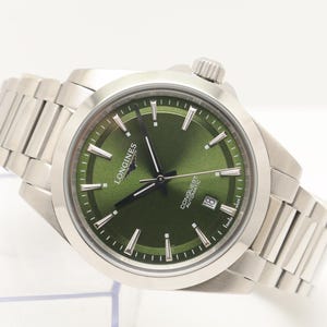 Op de afbeelding: Een roestvrijstalen Longines Conquest automatisch horloge met een zonnestraal groene wijzerplaat, zilverkleurige wijzers en uurmarkeringen, een datumvenster op de 6-uur positie en een geborstelde metalen schakelarmband met het Longines logo.