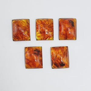 May include: Five rectangular cabochons with a warm, amber-like appearance. The cabochons have a mix of orange, yellow, and brown tones, with a glossy finish. The shapes are uniform, and the overall effect is of a natural, organic material.
