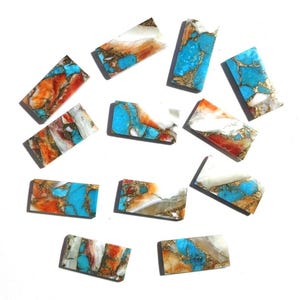 May include: A collection of rectangular gemstone cabochons. The stones feature a mix of colors, including turquoise, orange, white, and gold. The cabochons are arranged on a white surface, showcasing their unique patterns and textures.