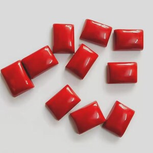 Pode incluir: Uma coleção de dez pedras preciosas retangulares, polidas, vermelho brilhante. As pedras preciosas estão espalhadas sobre uma superfície branca, cada uma com um acabamento brilhante. As formas são consistentes, sugerindo que são cortadas do mesmo material.