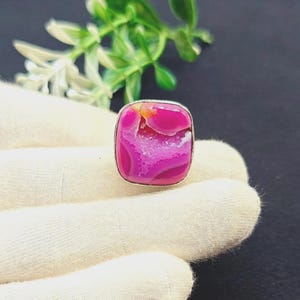 May include: A ring featuring a square-shaped, vibrant hot pink agate stone with a textured, crystalline center and a smooth, polished border. The stone is set in a simple silver-toned metal frame that highlights the deep magenta and fuchsia hues.
