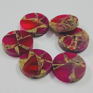 Op de afbeelding: Een verzameling van zeven ronde, gepolijste edelstenen. De stenen hebben een levendig rood en goud kleurenschema, met een mozaïekachtig patroon. De edelstenen worden waarschijnlijk gebruikt voor het maken van sieraden of knutselen.