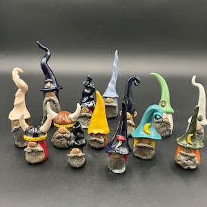 May include: A collection of ceramic gnomes with various colorful hats and beards. The gnomes have different hat styles, including pointed, curled, and horned designs. Each gnome has a unique color scheme, with hats in blue, yellow, green, and other colors.