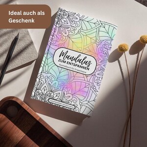 May include: A coloring book titled "Mandala's zum Entspannen" with a colorful, pastel-colored cover. The book features intricate black and white mandala designs. The cover text is in German. A pencil and decorative items are in the background.