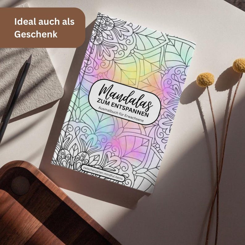 May include: A coloring book titled "Mandala's zum Entspannen" with a colorful, pastel-colored cover. The book features intricate black and white mandala designs. The cover text is in German. A pencil and decorative items are in the background.