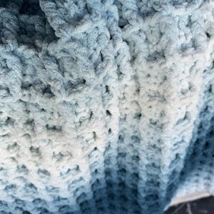 Peut inclure: Une couverture en crochet douce et moelleuse présentant un motif de couleur dégradé qui passe du bleu marine profond aux nuances plus claires de bleu et de blanc. Le textile affiche un motif de point gaufré texturé sur toute la surface.
