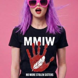 Könnte beinhalten: Schwarzes T-Shirt mit dem weißen Text "MMIW". Unter dem Text befindet sich ein roter Handabdruck mit einer weißen Feder. Am unteren Rand des Shirts steht "NO MORE STOLEN SISTERS".