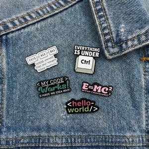 May include: A selection of enamel pins with tech and coding themes. The pins display phrases such as "Everything is Under Ctrl," "My Code Works!" and "Hello World." The pins are in various colours and shapes, including keyboard keys.