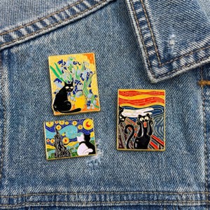 May include: Three enamel pins featuring famous art parodies. One pin depicts a black cat in front of a vase of flowers, another shows a cat in front of a starry night scene, and the third shows a cat in the style of The Scream.