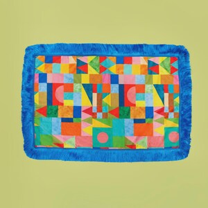 May include: A rectangular rug with a vibrant geometric design featuring squares, triangles, and circles in a variety of colours. The rug is trimmed with a bright blue fringe border.