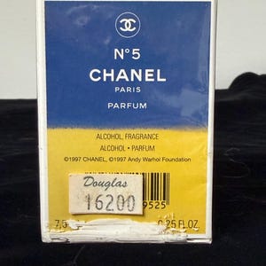 May include: A rectangular perfume box with a blue and yellow design. The box features the Chanel logo and the text "N&deg;5 CHANEL PARIS PARFUM." The box also includes the text "ALCOHOL FRAGRANCE ALCOHOL PARFUM" and "25 FL.OZ."