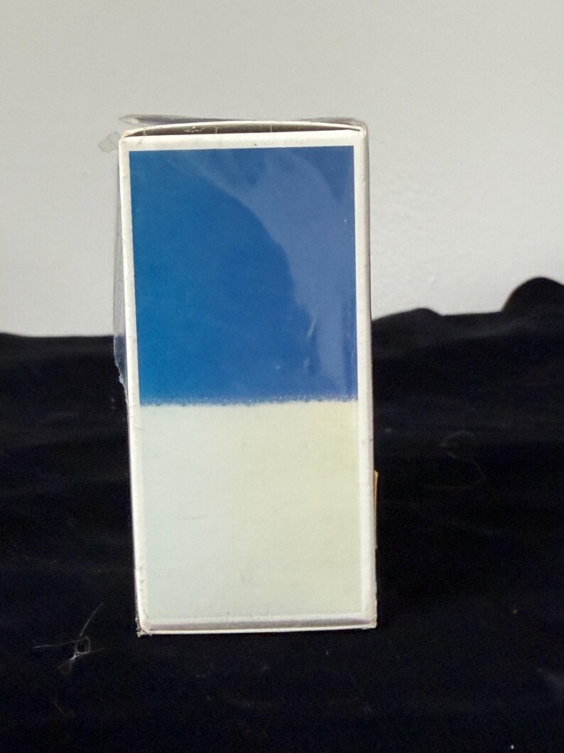 May include: A rectangular box with a two-tone design. The top half is a solid blue, and the bottom half is a light cream color. The box is wrapped in clear plastic.