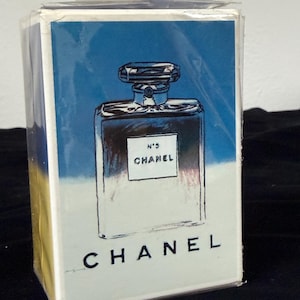 May include: A perfume box featuring a graphic illustration of a perfume bottle against a blue and white background. The box has the text "N&deg;5 CHANEL" in a rectangular white label and "CHANEL" at the bottom.