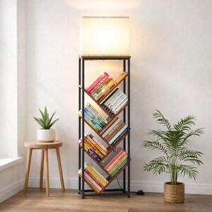 Pode incluir: Candeeiro de p&eacute; com estante integrada. O candeeiro tem um abajur retangular e uma estrutura de metal preto. A estante tem prateleiras de madeira com livros coloridos. Uma pequena planta em vaso est&aacute; numa mesa lateral de madeira.