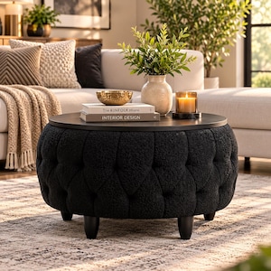 Pode incluir: Uma mesa de centro otomana redonda preta com capitonê e tampo de madeira escura. A mesa apresenta uma base de tecido texturizado com detalhes de botões e pernas pretas curtas. Dois livros intitulados The KINFOLK Home e INTERIOR DESIGN.