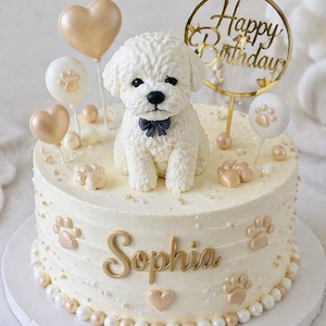 May include: A round, white iced birthday cake featuring a sculpted dog, paw prints, and heart-shaped balloons. The cake is inscribed with "Sophia" in gold and a gold "Happy Birthday" topper. The cake is decorated with gold and white pearls.