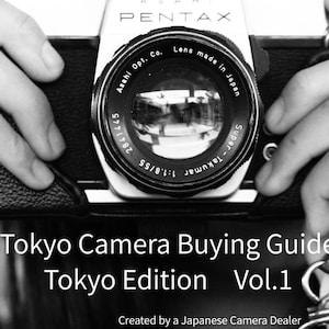 Könnte beinhalten: Schwarz-Weiß-Bild einer Vintage Pentax Kamera mit einem Objektiv, auf dem "Asahi Opt. Co." und "Lens made in Japan" steht. Die Kamera wird von Händen gehalten. Der Text "Tokyo Camera Buying Guide Tokyo Edition Vol.1" ist darunter zu sehen.
