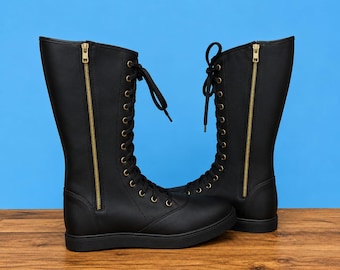 May include: A pair of black mid-calf boots featuring a lace-up front with gold-toned eyelets and black laces. Each boot includes a prominent vertical gold-toned zipper on the outer side, a rounded toe, and a flat black sole for a sleek, uniform look.