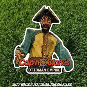 May include: A die-cut sticker featuring a bearded pirate character wearing a black tricorn hat, a yellow vest with gold buttons, and teal sleeves. The text reads Cap'n Clark's OTTOMAN EMPIRE with a ship's wheel graphic and BUY 5 GET 1 STICKER 2X2 FREE.