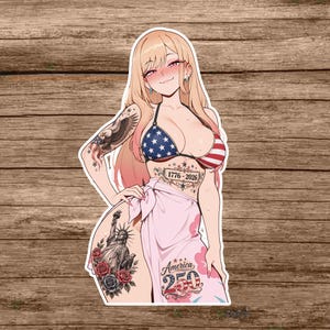 May include: A die-cut sticker featuring an anime-style character with long blonde hair, wearing a stars and stripes bikini and a pink sarong. The character has tattoos of a bald eagle, the Statue of Liberty, and text reading 1776-2026 and America 250.