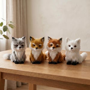 May include: Four plush fox figurines in grey, orange, reddish-brown, and white. Each fox has a fluffy appearance, with black accents on the ears and paws. They are arranged on a light brown wooden table.
