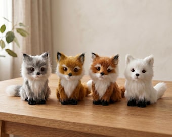 Puede incluir: Cuatro figuras de zorro de peluche en varios colores: gris, naranja, marrón rojizo y blanco. Cada zorro tiene una apariencia esponjosa, con detalles negros en las orejas y las patas. Están colocados sobre una mesa de madera marrón claro.
