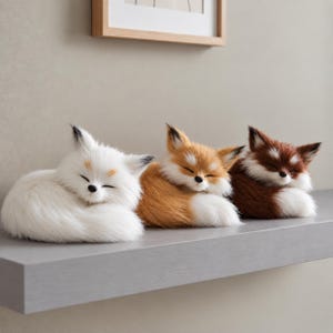 May include: Three plush fox figurines in a sleeping position, arranged in a row. The first is white, the second is orange and white, and the third is dark brown and white. Each fox has closed eyes, pointed ears, and a fluffy, textured appearance.