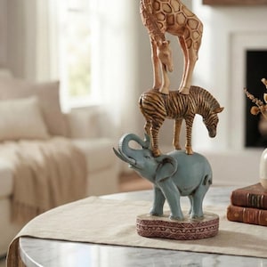 May include: A decorative figurine of stacked animals: a blue elephant, a zebra, and a giraffe. The figurine is displayed on a round table with a marble top. The figurine is a decorative item.