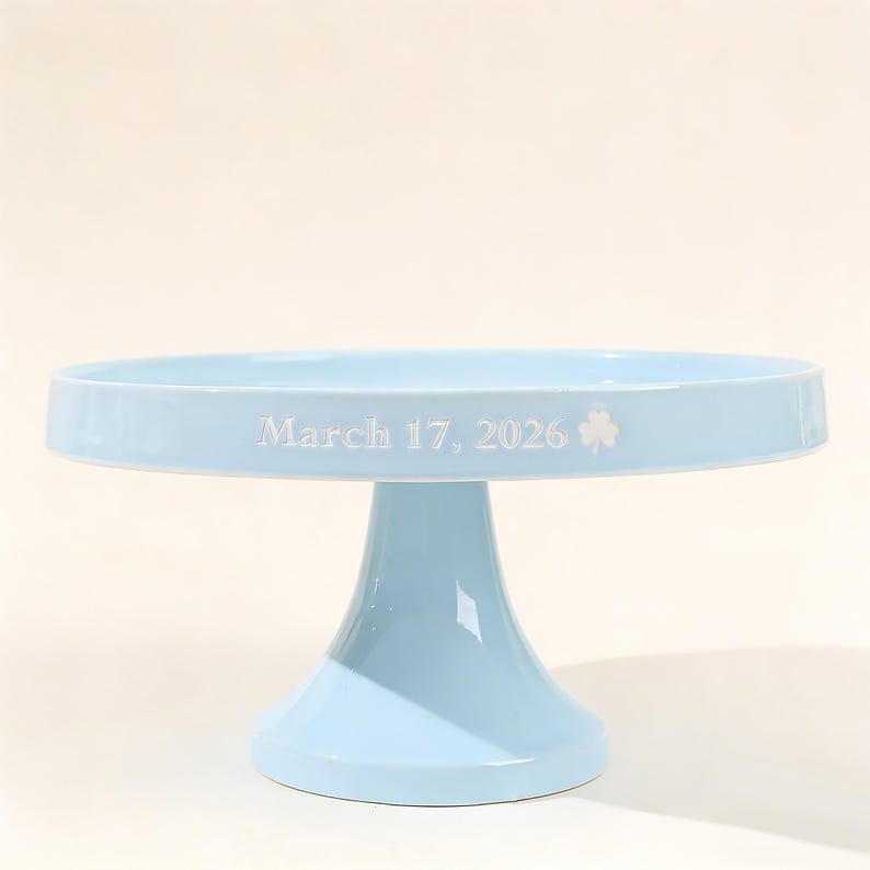 May include: A white ceramic mug with a black handle and the text "But First, Coffee" in a handwritten style. The mug is on a white surface. The mug is approximately 10 cm tall.