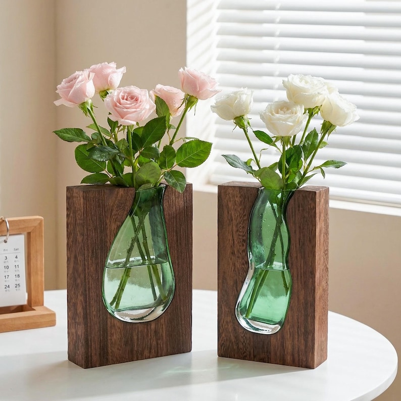 May include: Two wooden vases with a dark brown finish, each holding a green glass vase. The vases are filled with pink and white roses. The vases are on a white table.