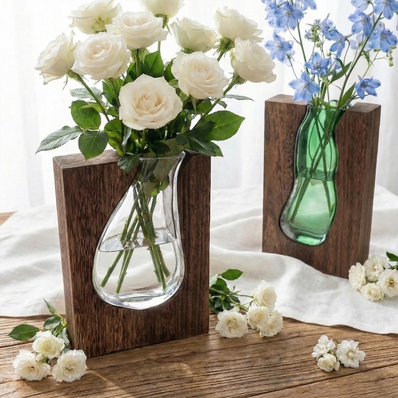 May include: Two wooden wall vases, one with white roses and the other with blue flowers. The vases have a clear glass insert. The wooden frames are rectangular and have a dark brown finish. The flowers are arranged in the vases.
