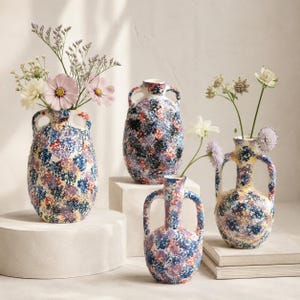 Peut inclure: Trois vases en céramique dotés de deux anses chacun, ornés d'un motif moucheté multicolore bleu, rouge, jaune et violet. Les vases sont présentés en différentes tailles, deux d'entre eux contenant des bouquets de fleurs rose pâle, blanches et violettes.
