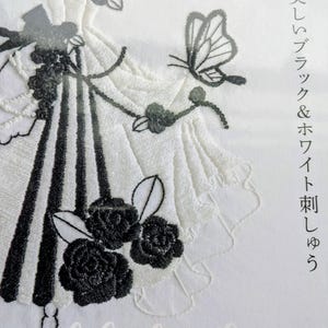 以下が含まれることがあります： 黒と白の刺繍デザイン。詳細なドレスを着たドレスフォームが特徴です。ドレスには黒の縦縞、黒の花柄のアクセント、蝶があります。「Black & White Embroidery」の文字が見えます。