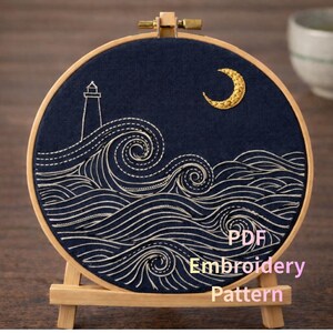 May include: An embroidery hoop featuring a navy blue fabric with a nautical design. The design includes a lighthouse, waves, and a crescent moon, all stitched in white thread. The text "PDF Embroidery Pattern" is visible.