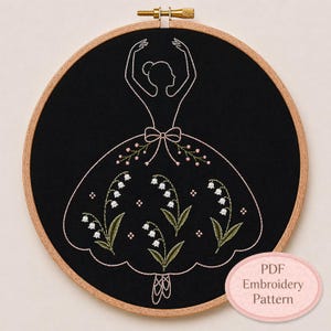 以下が含まれることがあります： 黒い布の刺繍枠にバレリーナのデザイン。 バレリーナは白い糸で縁取られ、スズランの花で飾られたドレスを着ています。 木製の枠で、テキスト「PDF Embroidery Pattern」はピンクの楕円形にあります。