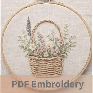 Op de afbeelding: Een ronde houten borduurring met een gebroken witte stof waarop een handgeborduurd ontwerp van een gevlochten mand vol wilde bloemen in roze, witte en paarse tinten staat. De tekst PDF Embroidery Pattern is zichtbaar op de afbeelding.