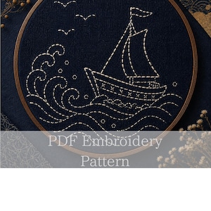 May include: A navy blue embroidery hoop featuring a sailboat design. The boat, waves, and birds are created with white thread. The text "PDF Embroidery Pattern" is displayed at the bottom of the image.