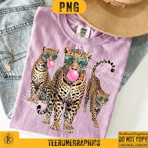 May include: A lilac Comfort Colors t-shirt featuring three leopard illustrations wearing sunglasses and blowing bubblegum bubbles. The shirt has the text "TeeRuneGraphics" at the bottom.