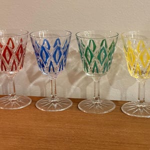 Puede incluir: Cuatro copas de vino transparentes con patrones de diamantes de colores en rojo, azul, verde y amarillo. Cada copa tiene un tallo largo y una base en forma de estrella. Miden unos 15 cm de altura.