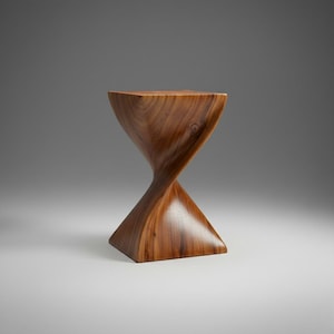 May include: A handcrafted wooden side table with a unique hourglass-like design. The table is made of a warm-toned wood, featuring a square top and base connected by a twisted, sculptural form. The wood grain is visible, adding to its natural aesthetic.