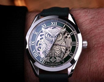 May include: A silver wristwatch with a green and silver face featuring an owl design. The watch has Roman numerals and a black leather band. The brand name "FLAGMAN&CO" is visible at the bottom of the watch face.