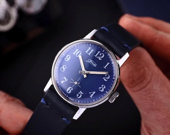 Könnte beinhalten: Eine Vintage-Armbanduhr mit dunkelblauem Zifferblatt und silbernen Zeigern und Ziffern. Die Uhr hat ein silbernes Gehäuse und ein dunkelblaues Lederarmband. Auf dem Zifferblatt steht das Wort "Gide".